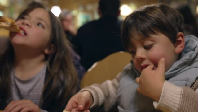 Children eating pizza at restaurant, siblings - little brother and sister enjoying carb food at diner in the evening