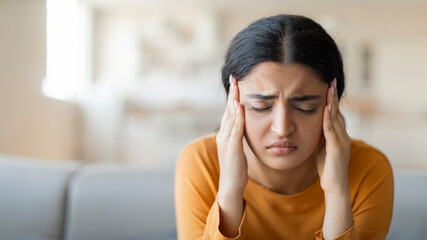 Stressed young indian woman suffering from severe headache or migraine at home