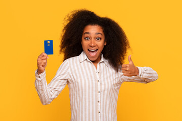 Excited black woman with credit card giving thumbs up on yellow background