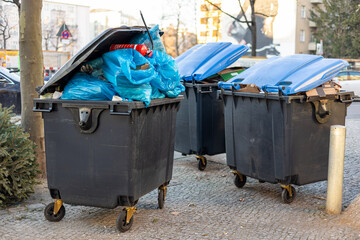 Überquellende Müllcontainer mit Abfall und Müllsäcken stehen auf dem Gehweg und warten auf die...