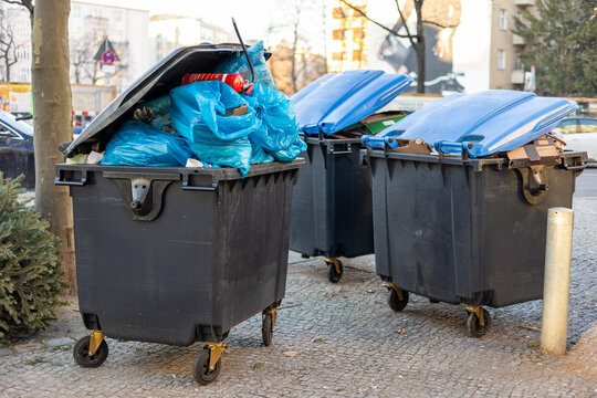 &Uuml;berquellende M&uuml;llcontainer mit Abfall und M&uuml;lls&auml;cken stehen auf dem Gehweg und warten auf die Abholung durch die M&uuml;llabfuhr