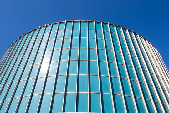 Glazed facade of a cylindrical building. Fragment of a building against a blue sky. Great for background.