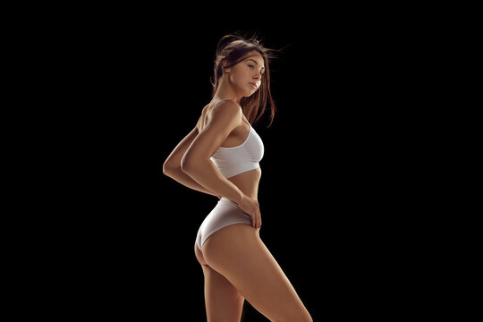 Side view image of slim, beautiful young woman posing in white cotton underwear against black studio background. Comfort. Concept of natural beauty, health and body care, fashion