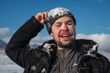 Young smiling man with snow on face portrait on mountains background in winter - 707297007