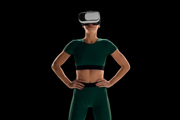 VR fitness equipment promotion and e-sport. Slim young woman wearing VR glasses and sportswear against black studio background. Concept of virtual sport, body and health care, innovations, technology