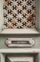 Close-up of an aged, green painted door with intricate metal grillwork and a letter slot