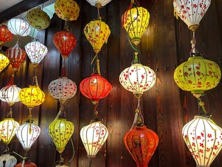 Selection of colorful paper lanterns suspended from the ceiling above a rustic wooden dining table