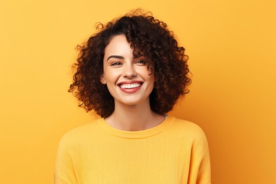 Portrait of a smiling young woman with curly hair over yellow background