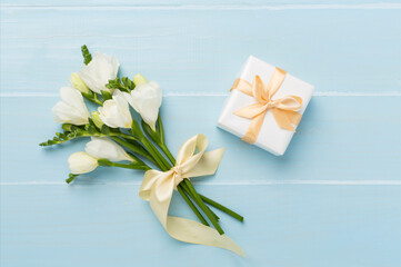 Gift box with freesia flower on wooden background, top view