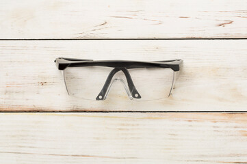 Safety glasses on wooden background, top view