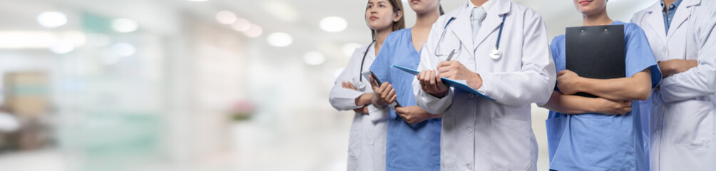 Confident medical staff team with doctor nurse and healthcare specialist professions people in blurry hospital corridor background. Medical and healthcare community in panoramic banner. Neoteric - obrazy, fototapety, plakaty