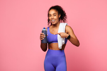 Sporty black lady in activewear holding towel and bottle, studio