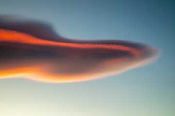 Firey, fluffy, lenticular cloud at sunset with blue sky