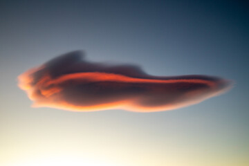 Grey lenticular cloud with firey red colours at sunset, isolated with blue sky