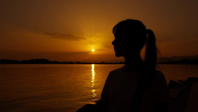 Silhouette of teenager admire sea dawn. A girl silhouette stand on the sea shore and look at the bright evening sun in summer.