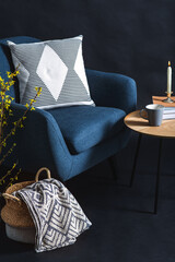 interior and home decor concept - close up of blue chair with pillow, blanket in wicker basket and tree branches in vase over black wall