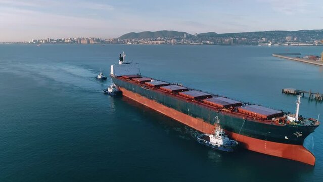 Huge cargo ship, towed by small towing boats, enters the port to load grain crops into dry holds and send the grain for export to Europe