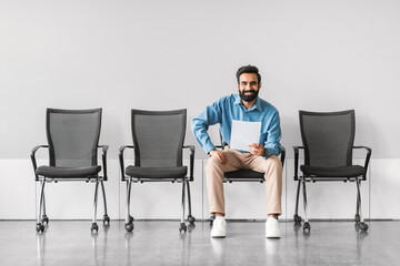 Smiling indian man sitting with document in a row of chairs