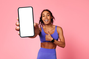 black sportswoman holding cellphone showing thumbs up over pink background