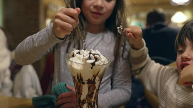 Little brother and sister eating ice cream sundae with whipped cream, family at weekend restaurant diner. children enjoy dessert