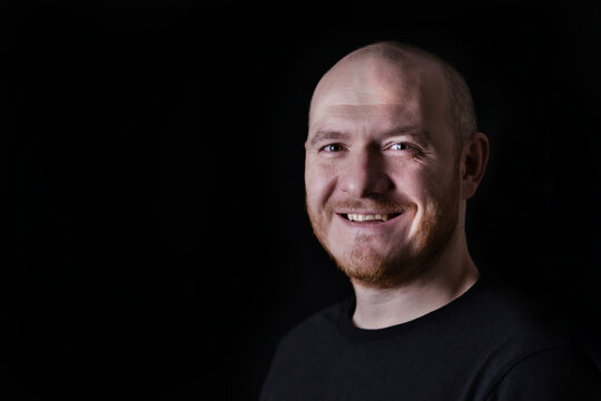 Portrait of smiling adult bald man on black background. Close up portrait of pleased white man in low key.