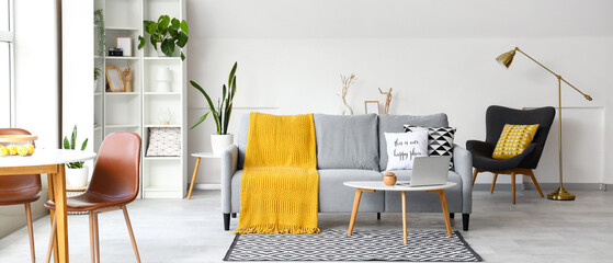 Interior of light living room with grey sofa and laptop on coffee table