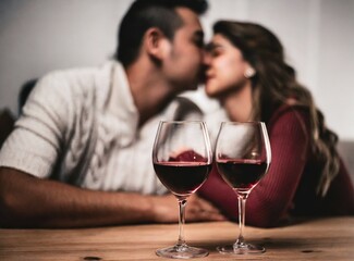 Couple kissing each other at home laying on the coach, with two glasses of red wine. Anniversary celebration.