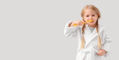 Cute little girl brushing teeth on light background with space for text