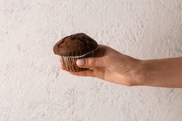 Woman holding tasty chocolate cupcake on light background