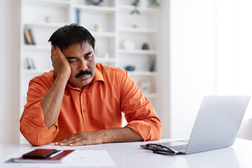 Sleepy middle aged indian man working at home office
