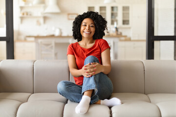 Obraz premium Cheerful young black woman sitting comfortably on a couch in living room