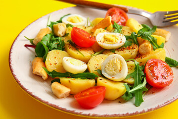 Plate of tasty potato salad with eggs and tomatoes on yellow background, closeup