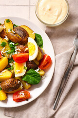 Plate of tasty potato salad with eggs and tomatoes on light background, top view