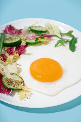 Plate with tasty fried egg and salad on blue background