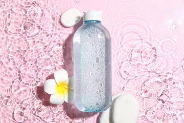 Poster Bottle of micellar water with spa stones and plumeria flower in water on pink background © Pixel-Shot