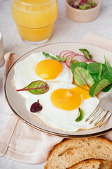 Plate with tasty fried egg, glass of juice, radish and spinach on light background