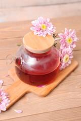 Transparent teapot with chrysanthemums on wooden table