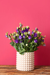 Vase with eustoma flowers on wooden table near red wall