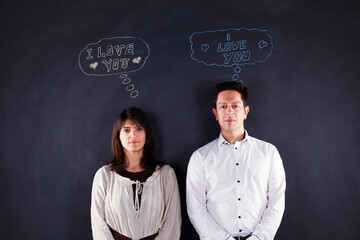 a young couple stands together in front of a chalkboard adorned with drawings of thoughts
