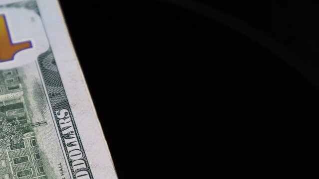 A closeup of 100 US dollar bank note, while rotating smoothly on an automatic table, keeping the text, security features and design of greenbacks in focus, 4K cinematic clip. 