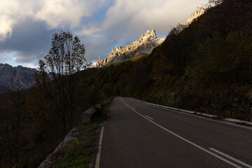 Landscape of Picos de Europa national park road through autumn forest with bright colorful leaves and sunset