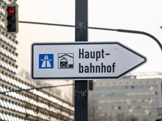 Hauptbahnhof (central station) sign guiding to the right in a city in Germany. Signpost for car drivers next to a traffic light. Inner city buildings are in the background.