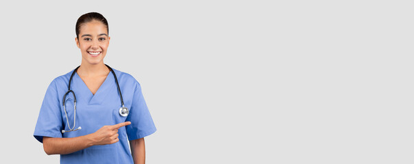 Friendly Caucasian millennial medical professional in blue scrubs pointing to the side