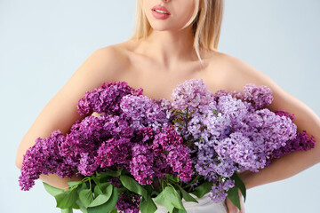 Naked young woman with lilac flowers on light background, closeup