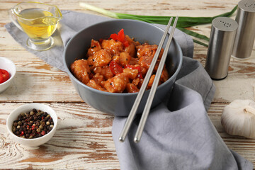 Tasty sweet and sour chicken in bowl with spices on light wooden background
