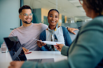 Happy multiracial couple giving their documents to insurance agent during meeting in office.