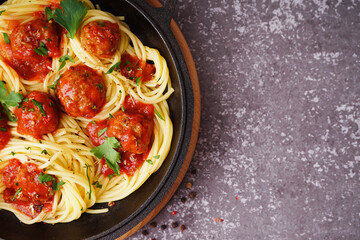 Frying pan of boiled pasta with tomato sauce and meat balls on grey table