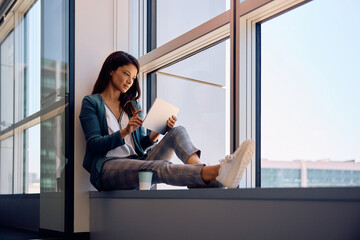 Female entrepreneur using digital tablet by window in office.