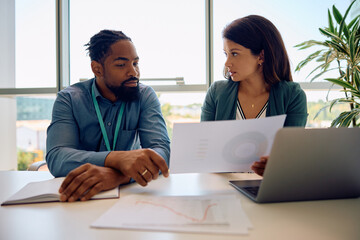 Black entrepreneur and his female colleague analyzing business reports on meeting in office.