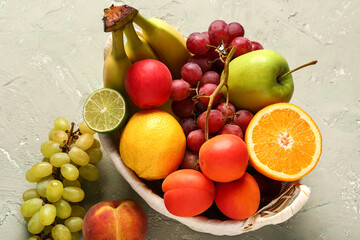 Wicker basket with different fresh fruits on grey background
